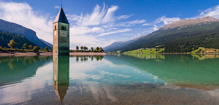 Die schönsten Alpenpässe mit dem Auto - Reschensee mit Kirchturm am Reschenpass in Tirol.